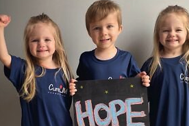 Tres niños con camisetas azul oscuro de Cure JM sostienen un cartel de esperanza