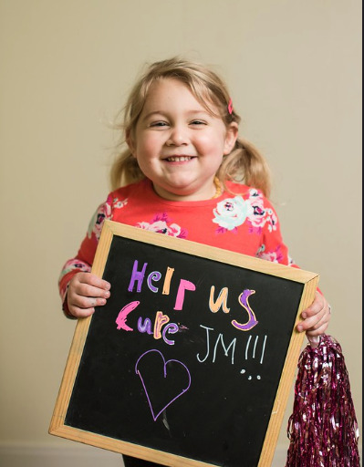 Young girl holds a "Help us Cure JM" sign.