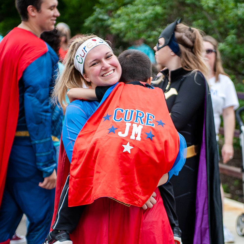 Smiling girl holding child in Cure JM superhero cape