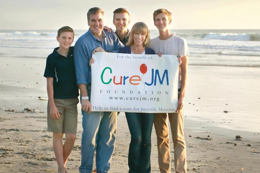 Family holding a Cure JM sign on a beach