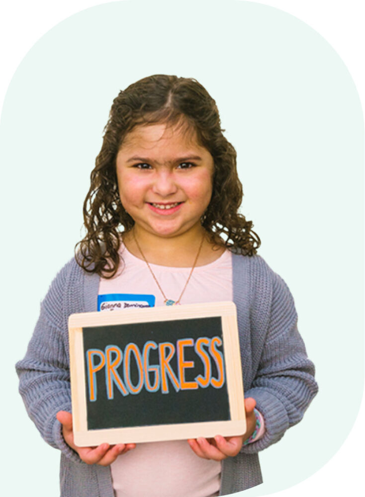 Young girl holding small chalkboard with the word "Progress" written on it.