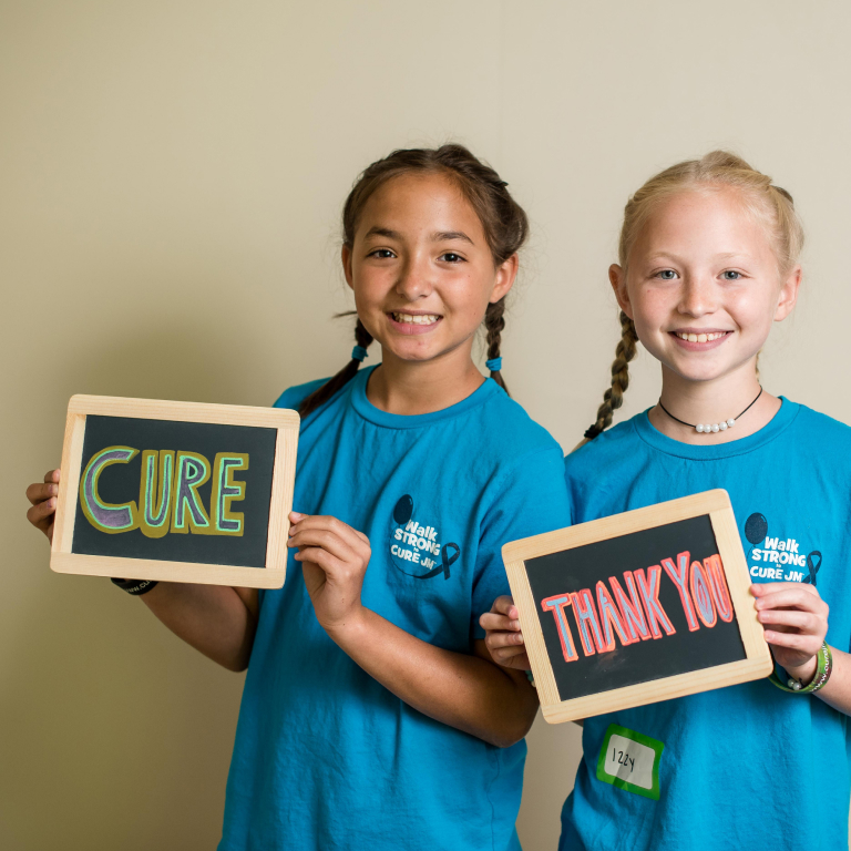Two girls holding chalkboard signs saying "Cure" and "Thank you"