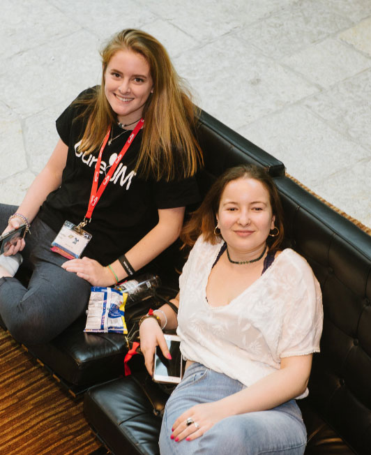 Mother and teenage daughter sit on a black couch.