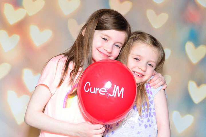 Dos chicas jóvenes sostienen un globo Cure JM.